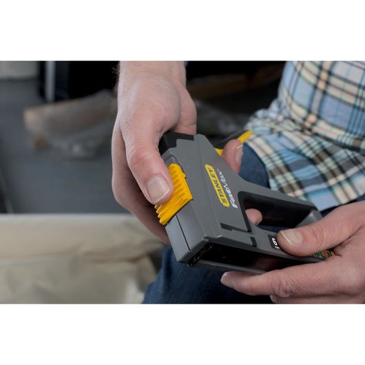 STANLEY FMHT0-70868 hand-held stapler with yellow slider, shown in use.