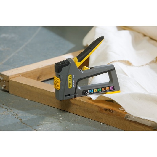 STANLEY FMHT0-70868 gray and yellow staple gun in use on wooden frame with white fabric.