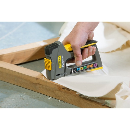 Stanley FMHT0-70868 staple gun used to fasten fabric to wooden frame, close-up angle, grey and yellow design.