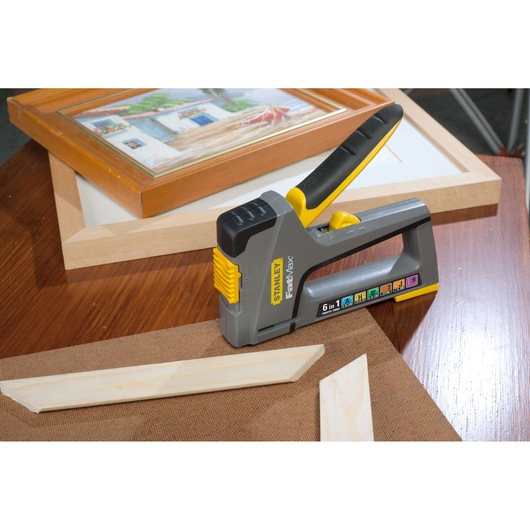 STANLEY FMHT0-70868 stapler, grey and yellow, shown on a wooden surface with picture frames and wood pieces.