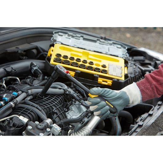 STANLEY FMHT0-74716 ratchet wrench in use on car engine, yellow socket set case in background.