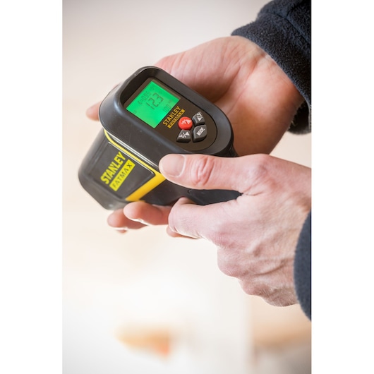 Photo of STANLEY FMHT0-77422 handheld digital measuring tool with LCD screen and control buttons in use.