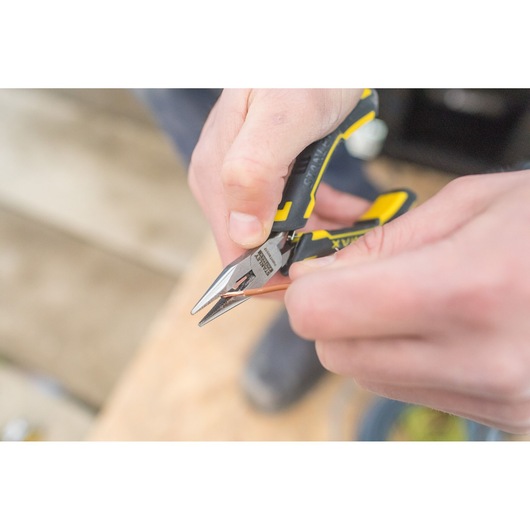 Stanley FMHT0-80517 pliers with yellow and black handle cutting copper wire, close-up photo.