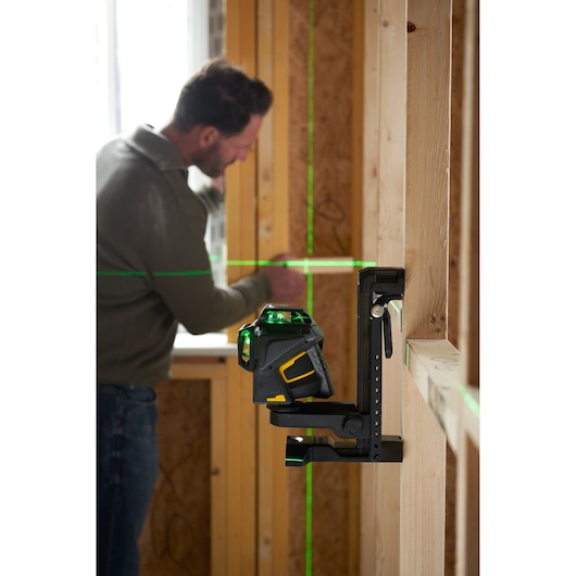 STANLEY FMHT1-77356 green beam laser level mounted on wall in construction setting, man working in background.