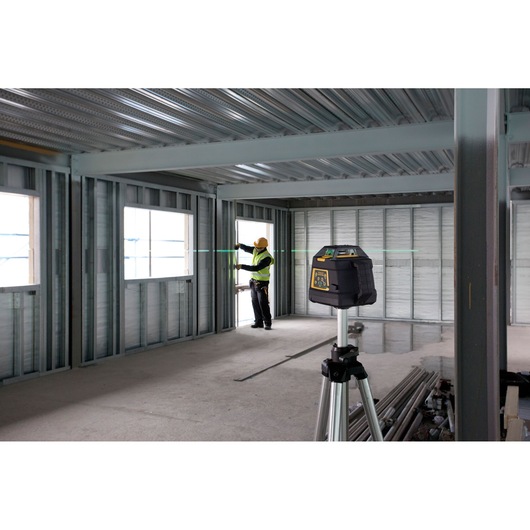 STANLEY FMHT1-77441 rotary laser on tripod in a steel-framed construction site with worker measuring alignment.