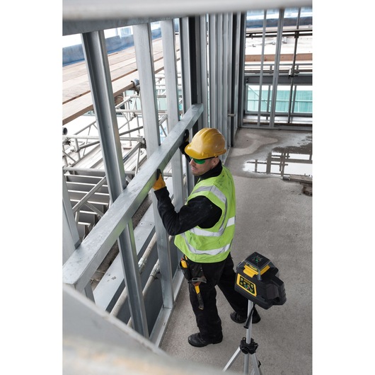 STANLEY FMHT1-77441 rotary laser level on tripod used by worker in safety gear at construction site.
