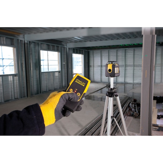 Photo of STANLEY FMHT1-77441 laser level and detector in a construction site, with tripod and worker's gloved hand.