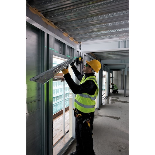 STANLEY FMHT1-77441 laser level used by a worker in a high-visibility vest and hard hat on a construction site.