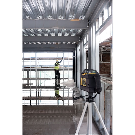 STANLEY FMHT1-77441 laser level on tripod in construction site, worker in background, interior view.