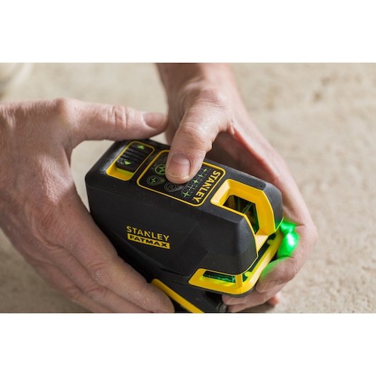 Photo of STANLEY FMHT1-77442 laser level being operated by hand, showing control buttons and green laser projection.