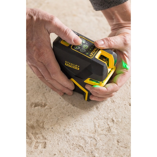 Photo of STANLEY FMHT1-77442 laser level in use on a beige surface, hands adjusting black and yellow tool.