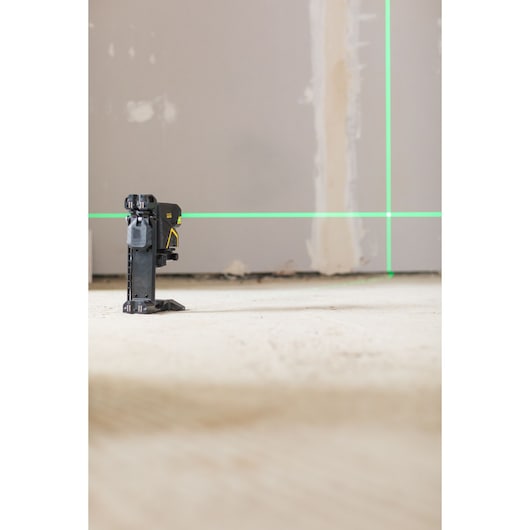 STANLEY FMHT1-77442 laser level projecting green lines, side angle, on unfinished floor and wall.