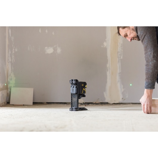 STANLEY FMHT1-77442 laser level on tripod in construction site, wall and worker stacking tiles in background.