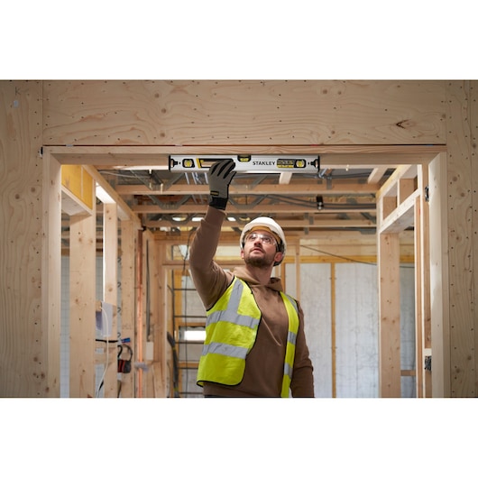Worker uses STANLEY FMHT43673-1 spirit level in wooden doorway frame on construction site.