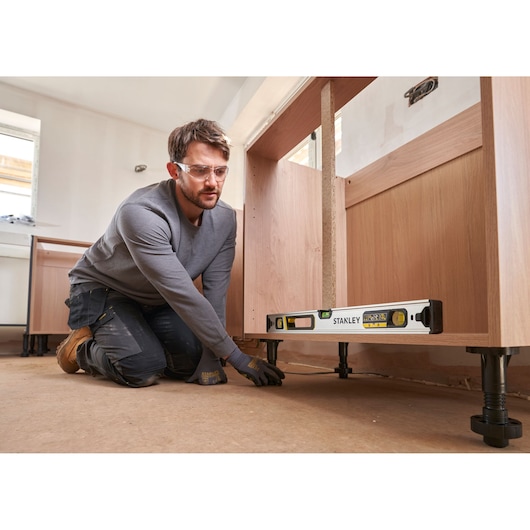 Photo of a person using a STANLEY FMHT43673-1 spirit level to adjust cabinet legs during kitchen installation.