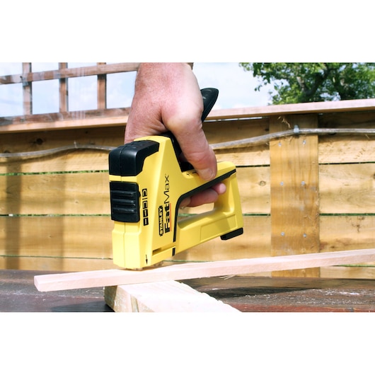 Photo of STANLEY FMHT6-70411 staple gun in use, yellow and black, shown fastening wood outdoors.
