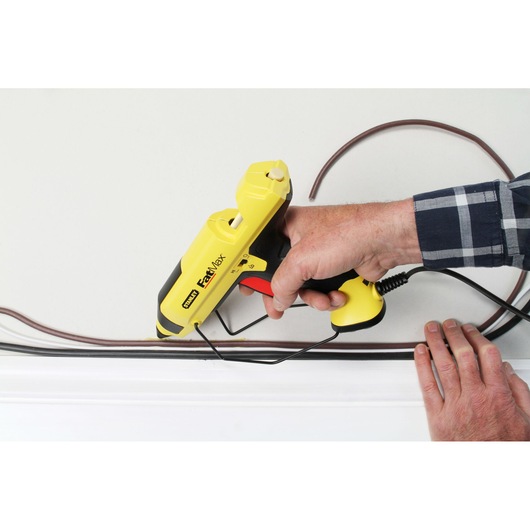 STANLEY FMHT6-70418 yellow FastMax glue gun in use for cable installation on a wall.