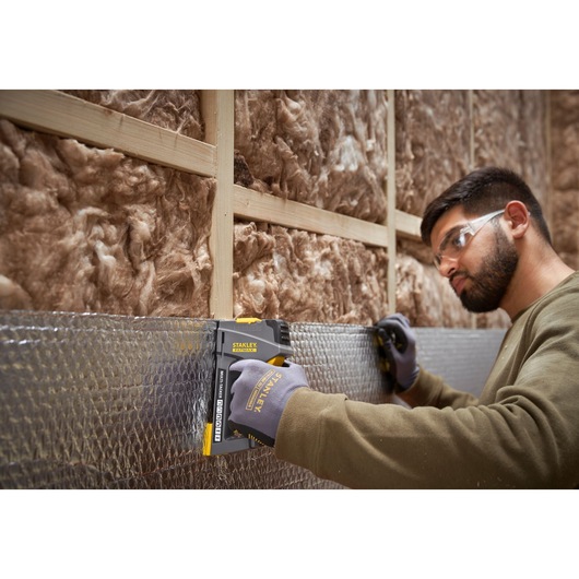 STANLEY FMHT6-70868 staple gun used on insulation by gloved worker, shown in construction setting.