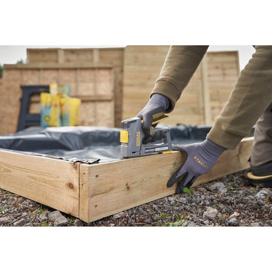 STANLEY FMHT6-70868 multi-tacker stapler used on wooden garden bed in outdoor setting.