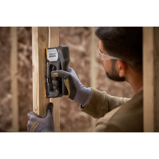 STANLEY FMHT70401-0 stapler used by gloved hands to secure wire to wood frame.