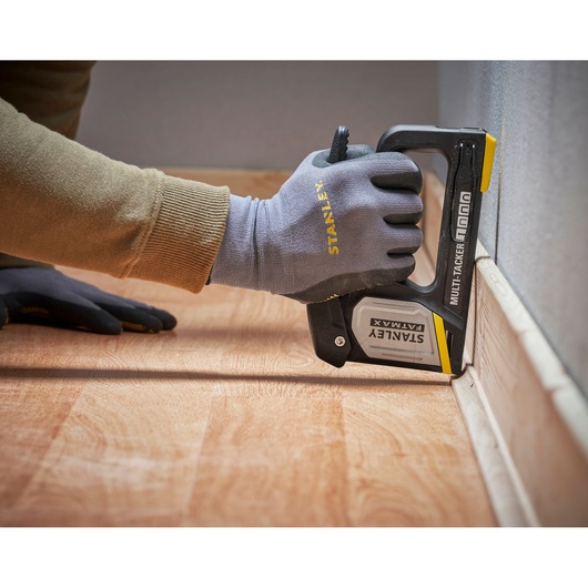 STANLEY FMHT70401-0 multi-tacker stapler in use securing flooring near wall, shown in close-up.