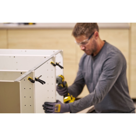 STANLEY FMHT83270-0 bar clamps securing white cabinet panels during assembly, close-up, workshop setting.