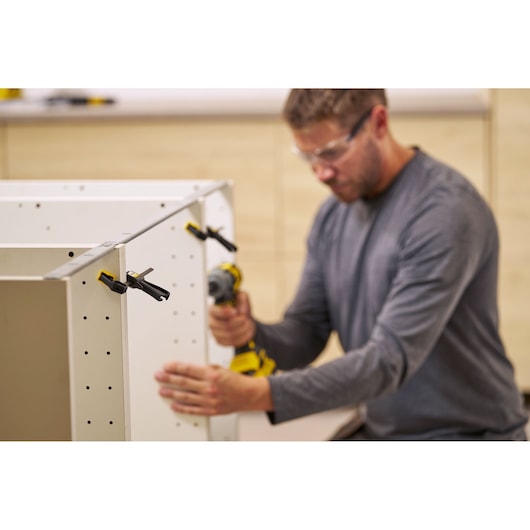 STANLEY FMHT83270-0 clamp securing white cabinet panels during assembly, person using power drill.