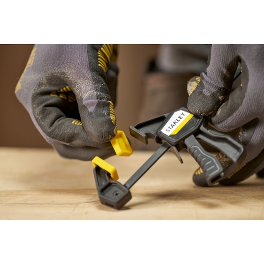 STANLEY FMHT83270-0 photography of black and yellow hand clamp held by gloved hands on a wooden surface.