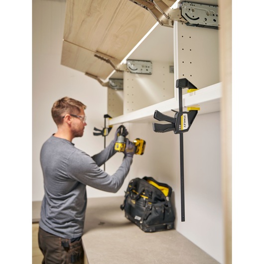 STANLEY FMHT83272-0 quick-adjust bar clamp holding shelf during installation, workshop setting.