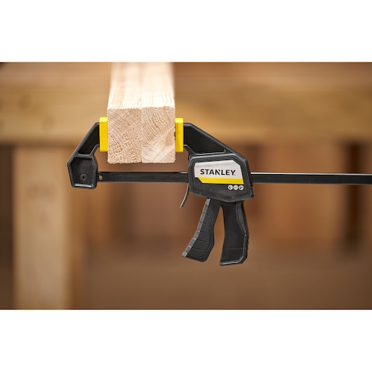 STANLEY FMHT83272-0 trigger clamp securing two wooden boards, side view, yellow and black design.