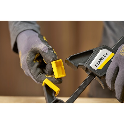 STANLEY FMHT83272-0 trigger clamp close-up with yellow removable jaw pad, held by gloved hands.