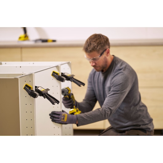 STANLEY FMHT83273-0 clamps securing white cabinet panels during assembly, close-up, workshop setting.