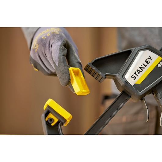 STANLEY FMHT83273-0 clamp with detachable yellow pad, close-up angle, person wearing gloves.