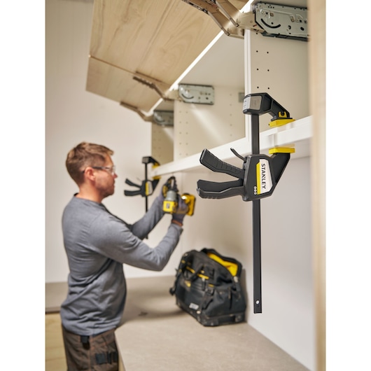 Photo of STANLEY FMHT83274-0 bar clamp in use during cabinet installation, tool bag visible on counter.