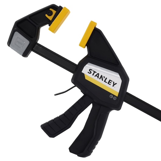 Photo of STANLEY FMHT83274-0 trigger clamp with black body and yellow pads, side angle on white background.