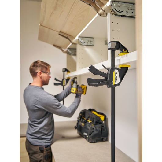 Photo of STANLEY FMHT83275-0 bar clamp holding a white shelf during installation in a workshop.