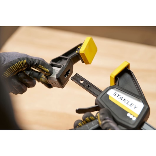 Photo of STANLEY FMHT83275-0 clamp with yellow pads, held by gloved hands, close-up side angle.