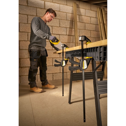 Photo of STANLEY FMHT83276-0 bar clamps securing wood on workbench, used by worker in workshop.