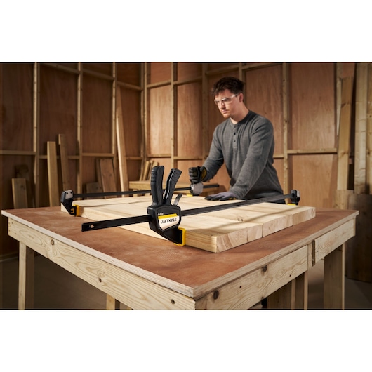 STANLEY FMHT83277-0 bar clamp securing wood pieces on a workbench in a workshop setting.