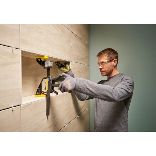 STANLEY FMHT83278-0 clamp used for tile installation on a wall, person wearing gloves.