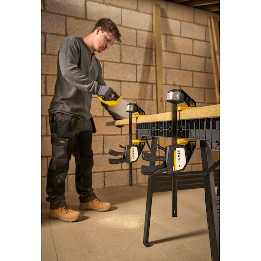 Photo of STANLEY FMHT83279-0 bar clamps securing wood to a workbench in a workshop setting.
