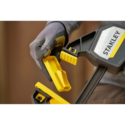 STANLEY FMHT83279-0 clamp close-up, yellow and black jaws, gloved hand adjusting clamp.