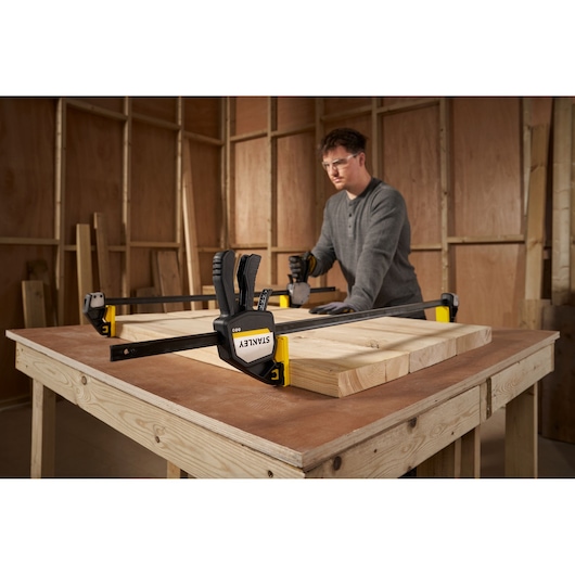STANLEY FMHT83282-0 bar clamp holding wood boards on a workbench, workshop background.