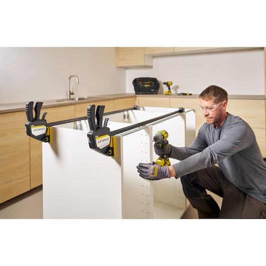 Photo of STANLEY FMHT83282-0 clamps securing white cabinet panels during assembly in a kitchen setting.