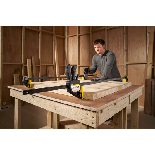 STANLEY FMHT83283-0 large bar clamp securing wooden boards on workbench in woodworking shop.
