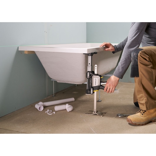 Photo of STANLEY FMHT83554-1 bar clamp holding bathtub frame during installation, plumber adjusting corner.