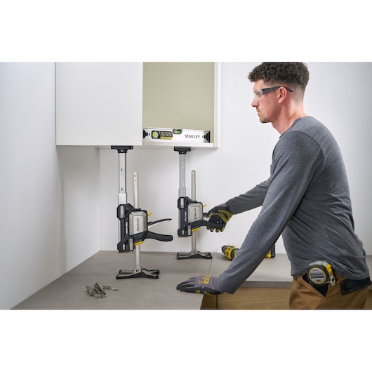 STANLEY FMHT83554-1 clamp holding cabinet in place on worktop, side view, worker adjusting clamp.