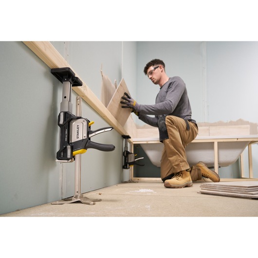 STANLEY FMHT83554-1 clamp securing wood to a wall during construction, person installing tiles in bathroom.