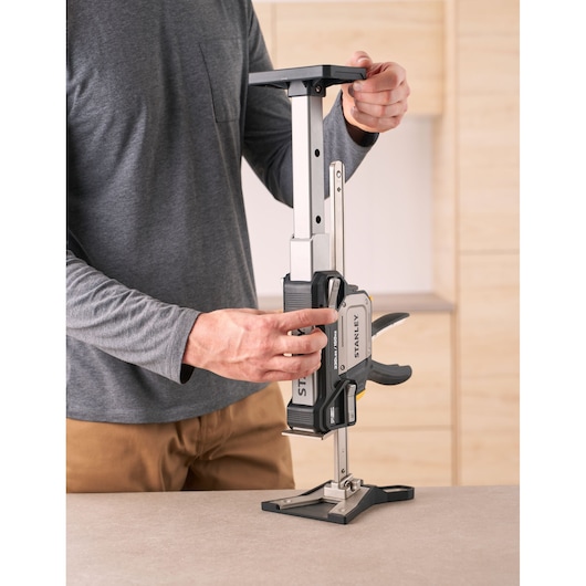 Photo of STANLEY FMHT83554-1 support clamp being adjusted on a tabletop, operator in grey shirt visible.