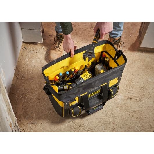 STANLEY FMST1-71180 tool bag filled with hand tools and accessories, top view, on construction site floor.